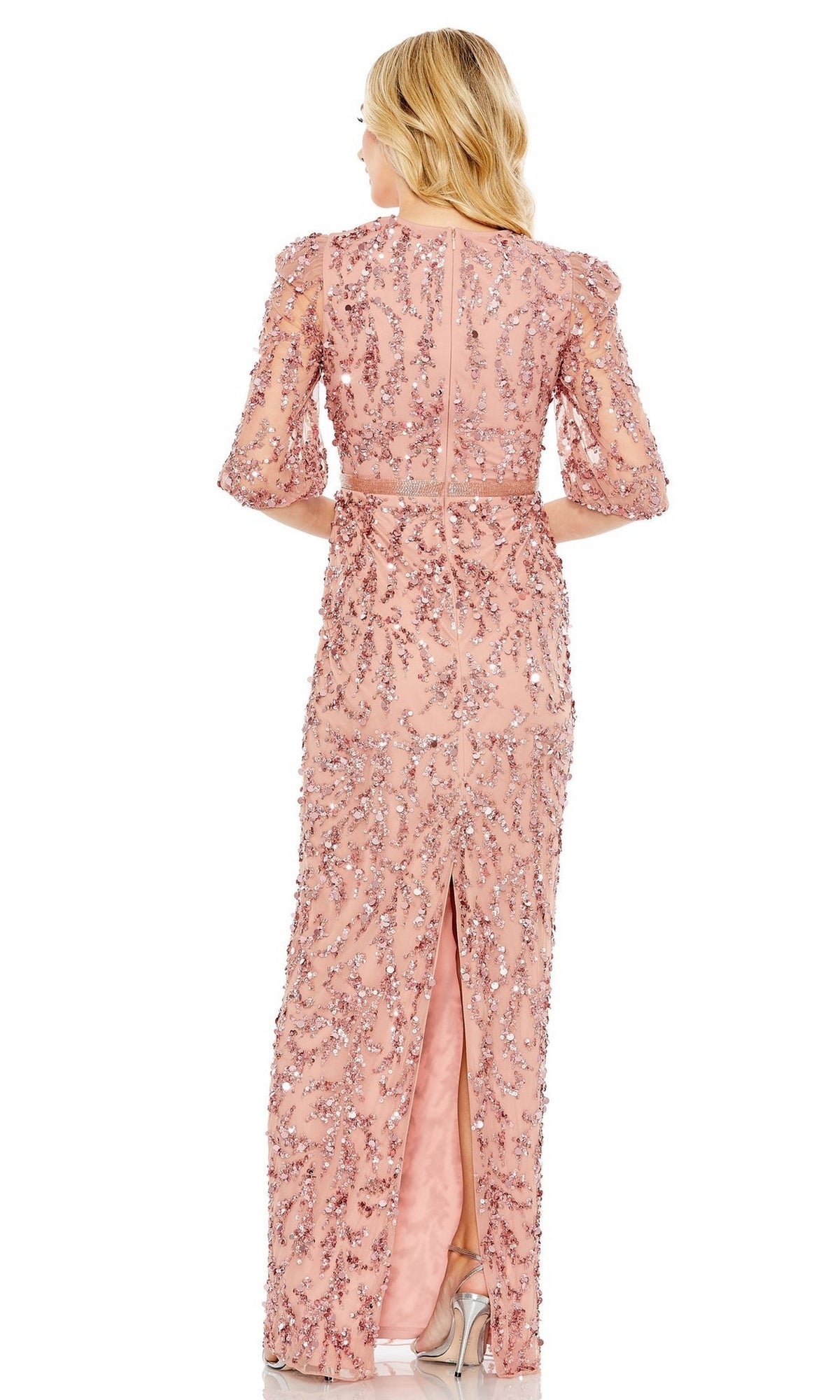 A woman in a light pink Mac Duggal 93790 Long Sleeve Beaded Formal Dress stands facing away, highlighting the gown's sparkling sequins, back slit, and elegant long sleeves.